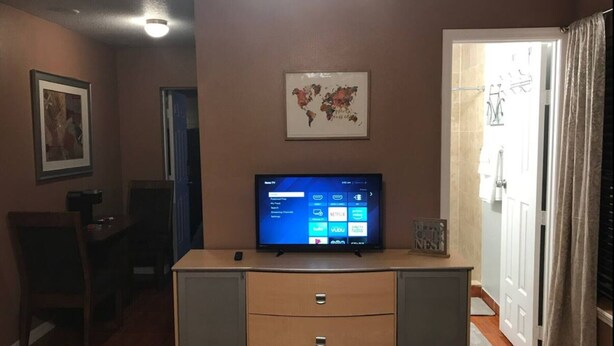 A living room with a flat-screen TV on a wooden cabinet, a framed world map on the wall, and a door leading to another room. - Charming studio in delightful Orlando with WiFi and AC (Orlando)