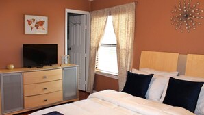A bedroom with a bed, a television on a dresser, a door, and a window with curtains. - Charming studio in delightful Orlando with WiFi and AC (Orlando)