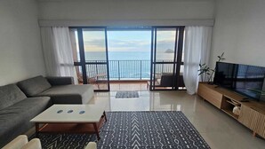 A modern living room with a sofa, coffee table, and TV, large windows with a view of the sea, and a balcony with outdoor furniture. - Charming apartment with sea view in Copacabana (Ipanema Rio de Janeiro)