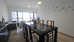 A modern living room with a glass dining table, black chairs, a sofa, and a large window with curtains. - Charming apartment with sea view in Copacabana (Ipanema Rio de Janeiro)