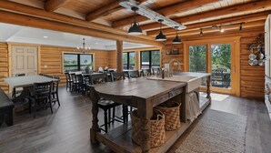 A spacious log cabin interior with a large dining area, multiple windows, and a kitchen area. - Snowberry Inn: Large Kitchen & Gathering Room 9BR 11BA Ensuite bath in all rooms (Eden)