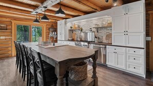 A rustic kitchen with wooden beams, a large island, white cabinets, and hanging pendant lights. - Snowberry Inn: Large Kitchen & Gathering Room 9BR 11BA Ensuite bath in all rooms (Eden)
