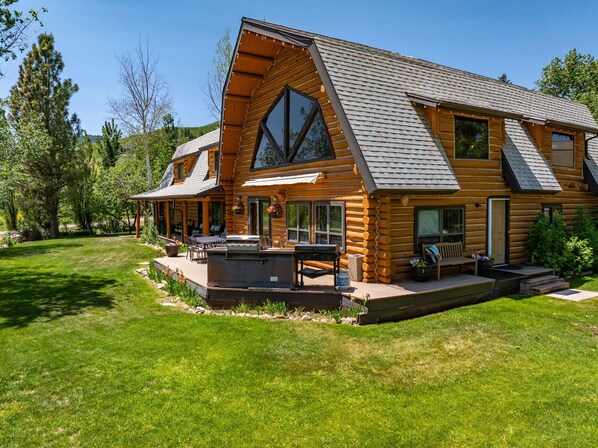 Una cabaña de troncos con una amplia terraza, mobiliario exterior y un patio cubierto.
