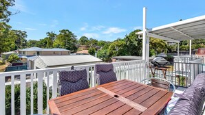 Een houten terras met een tafel, stoelen en een barbecue, omringd door een witte schutting.