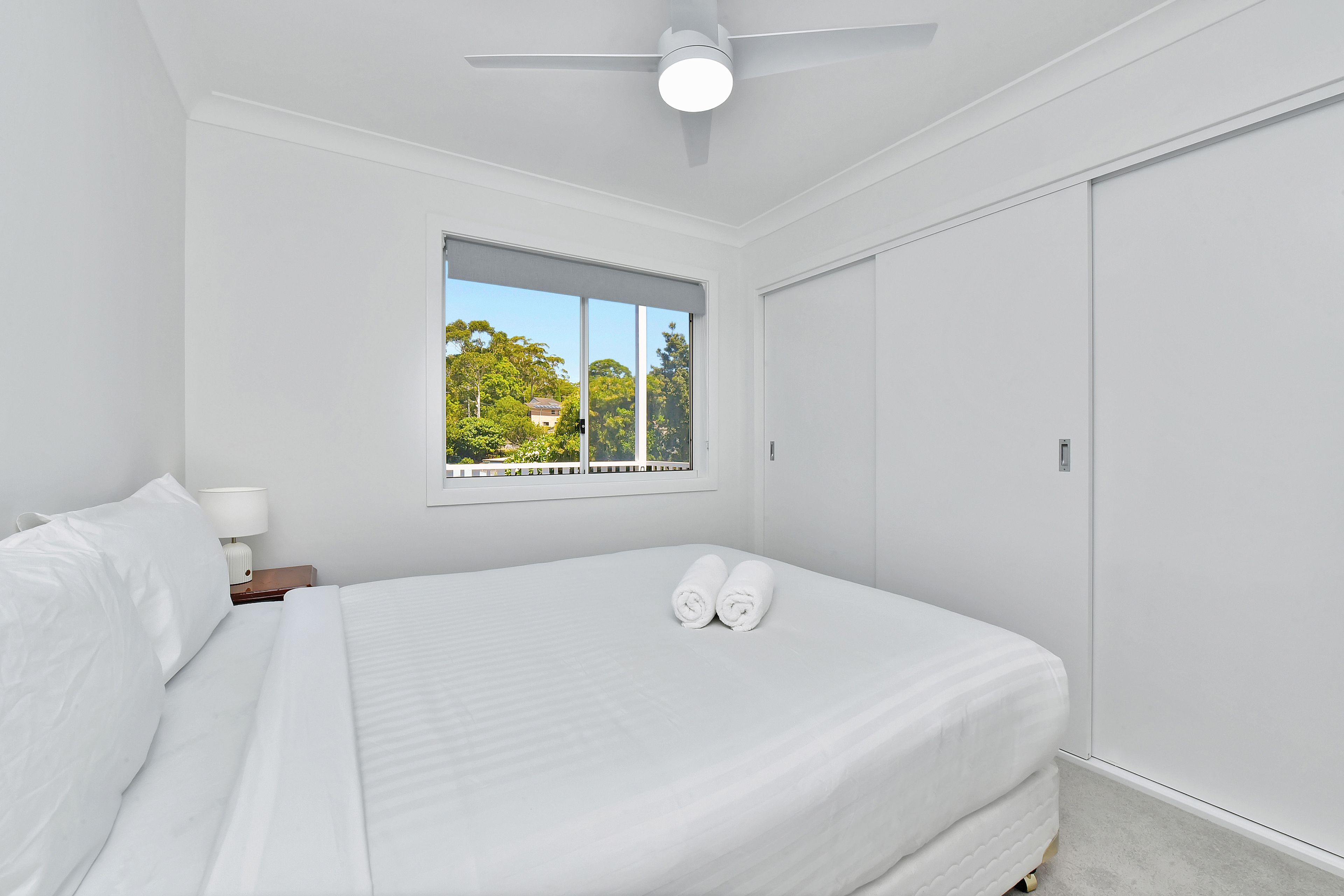 A bedroom with a bed, a window with a view of trees, a ceiling fan, and a wardrobe.