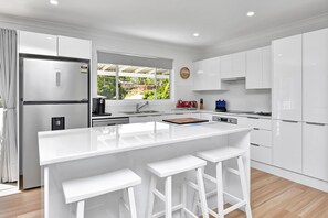 A modern kitchen with white cabinetry, a central island with stools, a built-in oven, and a window overlooking a residential area.
