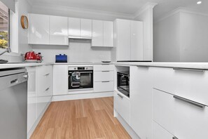 A modern kitchen with white cabinetry, a built-in oven, and a coffee machine.