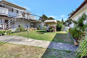 A residential property with a covered outdoor area, a staircase leading to a balcony, and a variety of potted plants.