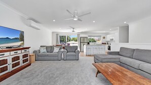 A modern living room with grey sofas, a wooden coffee table, and a TV displaying a beach scene.