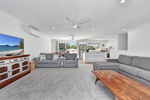A modern living room with a television, grey sofas, a wooden coffee table, and a kitchen in the background.