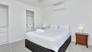 A modern bedroom with a single bed, bedside tables, a wardrobe, and an air conditioning unit.