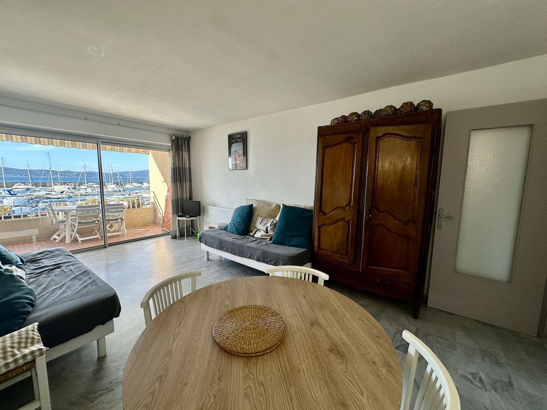 A room with a balcony, a sofa, a dining table, and a wardrobe.