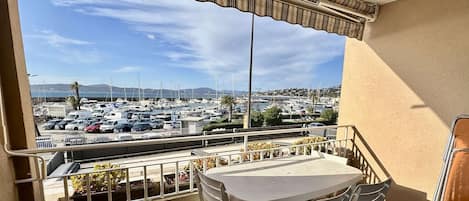 A balcony with a table and chairs, a view of a marina with boats, and a parking lot.