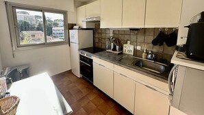 A kitchen with white cabinets, a black countertop, a window with a view of buildings, and a hanging pot rack. - APARTMENT FOR 4 PEOPLE IN A RESIDENCE WITH POOL NEAR THE SEA  AND TOWN CENTER (STE MAXIME)