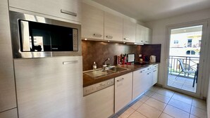 A modern kitchen with stainless steel appliances, a built-in microwave, and a large window overlooking a balcony. - APARTMENT T3 AIR-CONDITIONED FOR RENT FOR 4 PEOPLE IN THE CITY CENTER (STE MAXIME)