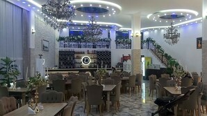 A restaurant with multiple dining tables and chairs, a bar area with a wine rack, and a staircase leading to an upper level. - Hotel zurapalace (Batumi)