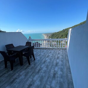 Un balcon avec une table et des chaises, offrant une vue sur la côte, avec des bâtiments et de la végétation.