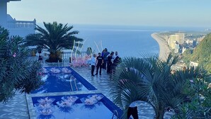 A pool with water lilies, palm trees, and a view of the sea and buildings. - Hotel zurapalace (Batumi)
