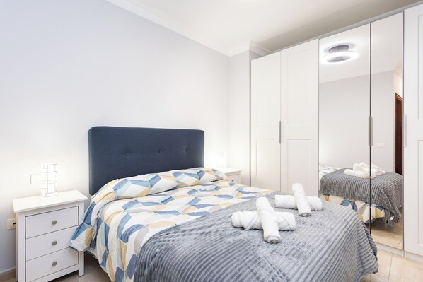 A bedroom with a bed, a nightstand, a wardrobe, and a mirror.