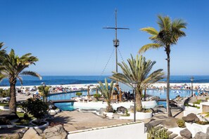 A resort pool area with palm trees, lounge chairs, and a view of the ocean.