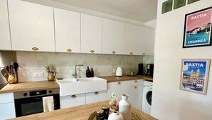 A modern kitchen with white cabinets, a wooden countertop, a sink, and a washing machine. There are decorative items on the countertop and a framed picture on the wall. - Villa Caline | Wi-Fi, Clim, 150 m from the beach (Lucciana)