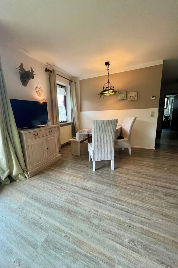 Una sala de estar con televisor, un mueble de madera, una silla y una lámpara colgante.