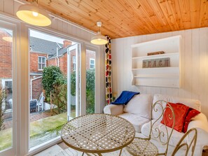 A room with a white sofa, a round wicker table, and a wooden ceiling. There are white walls and a brick exterior visible through the windows. - 2 bedroom accommodation in Weymouth (Weymouth)