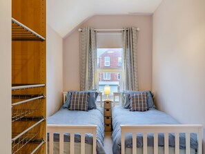 A bedroom with two beds, a window with curtains, a radiator, and a wooden wardrobe. - 2 bedroom accommodation in Weymouth (Weymouth)