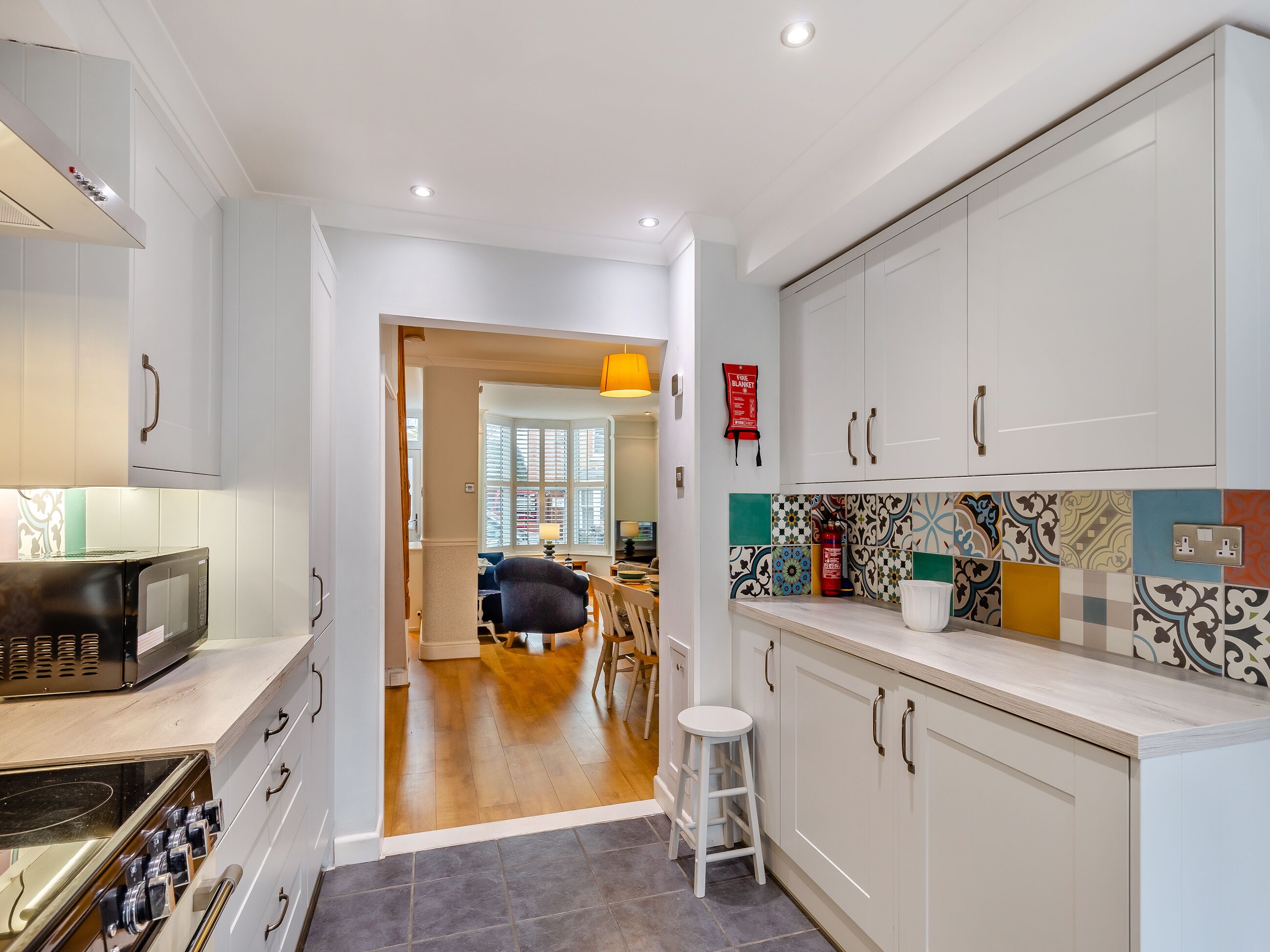 A modern kitchen with white cabinets, a microwave, and a wooden dining area visible through an open doorway.