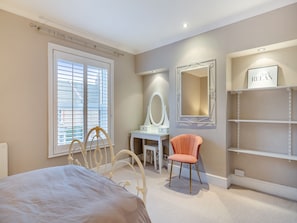 A bedroom with a bed, a vanity with a mirror, a chair, and a shelf with a sign. - 2 bedroom accommodation in Weymouth (Weymouth)