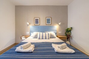 A hotel room with a bed, two wall-mounted lamps, a nightstand, a potted plant, and two framed pictures on the wall. - SOLIS MARE Apartments - Palo Beach (Málaga)