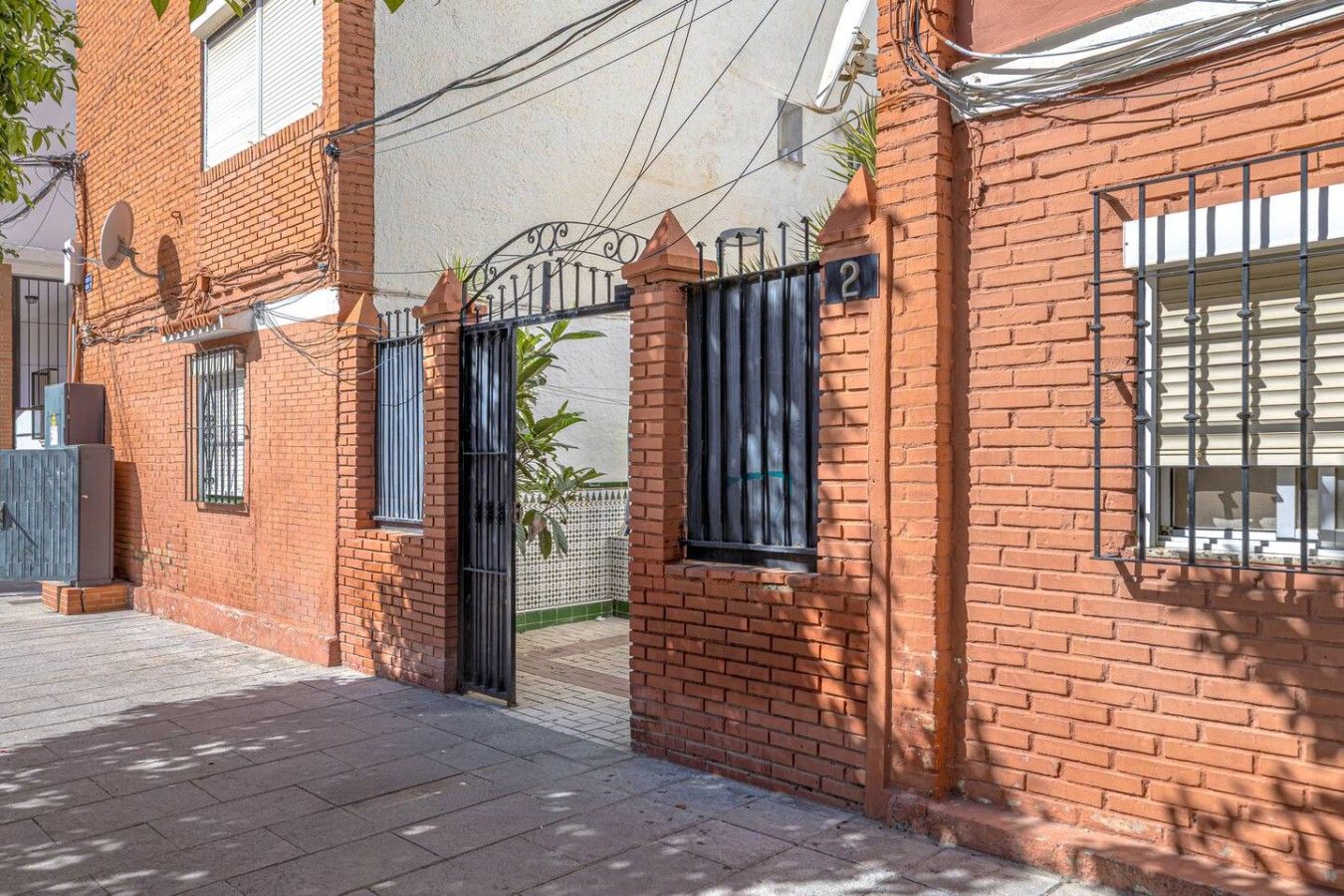Un edificio de ladrillo con entrada protegida por una reja, numerado 2, y una antena parabólica en el techo.