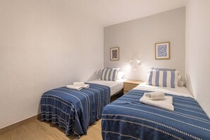 Une chambre d’hôtel avec deux lits, chacun recouvert d’une courtepointe bleue et blanche à rayures, un mur blanc et un tableau encadré au-dessus des lits.