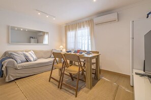 A compact living space with a sofa, a dining table with chairs, a TV, and an air conditioning unit. - SOLIS MARE Apartments - Palo Beach (Málaga)