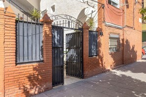 A gated entrance with a metal gate, brick walls, and a paved sidewalk. - SOLIS MARE Apartments - Palo Beach (Málaga)