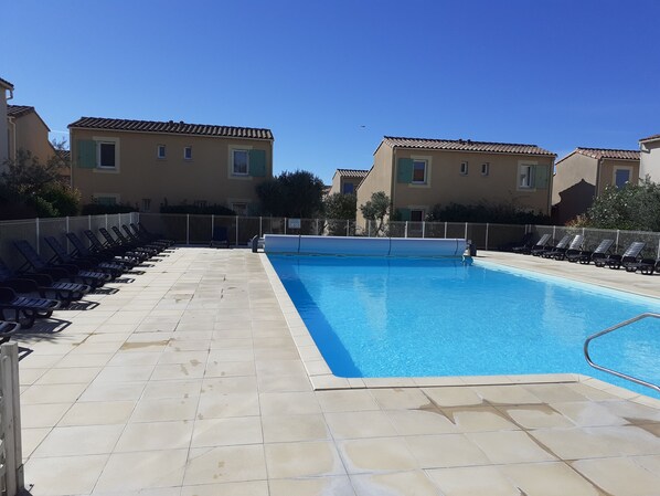 Una piscina con suelo de baldosas y sillas de descanso.