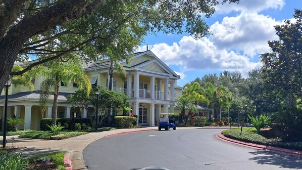 A large, yellow colonial-style house with a porch and multiple windows, surrounded by lush greenery and a clear blue sky.