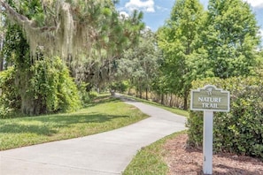 A nature trail sign with a pathway surrounded by trees and greenery.
