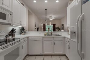 A modern kitchen with white cabinetry, a built-in microwave, a coffee maker, and a dishwasher.