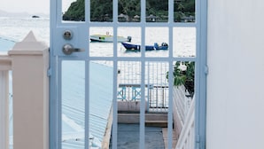 Une vue à travers une grille métallique, avec une terrasse en bois menant à un balcon surplombant une étendue d’eau où se trouvent des bateaux.