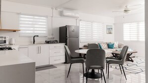 Une cuisine moderne avec des meubles blancs, un réfrigérateur noir et un coin repas comprenant des chaises grises et une table blanche.
