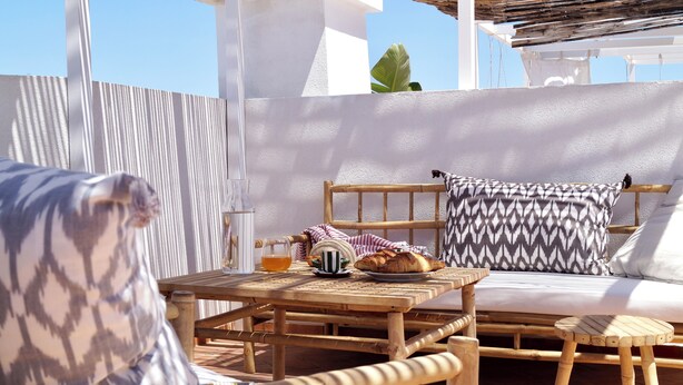 Un espacio de estar al aire libre con muebles de mimbre, una mesa, sillas y un banco acolchado.
