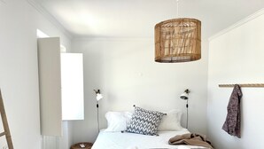 Un dormitorio moderno con una cama, dos lámparas de noche, una lámpara colgante de ratán, una escalera de madera, una mesita de noche de mimbre y una toalla sobre la cama.