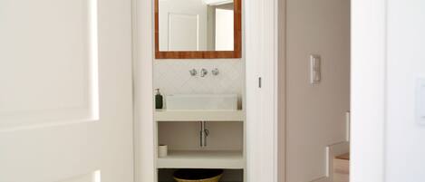 Une salle de bain avec un lavabo blanc, un miroir avec un cadre en bois et un carrelage décoré.