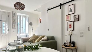 A modern living room with a green sofa, a glass jar with bread on a woven placemat, and a small table with a plant and a coffee maker.