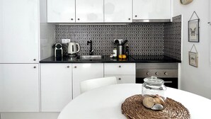 A modern kitchen with white cabinets, a black countertop, a patterned backsplash, and a clock on the wall.