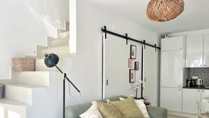 A modern living room with a green sofa, a black floor lamp, and a kitchen area with white cabinets.