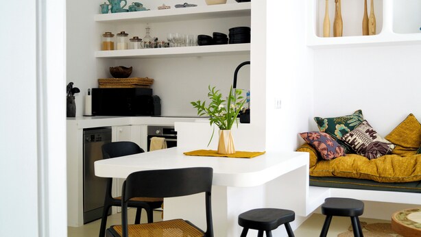 A modern kitchen with white cabinetry, a dining area with a white table and black chairs, and a living area with a sofa and cushions. - Casa Pasha - Olhão, Algarve (Olhão)