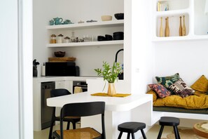 A modern kitchen with white cabinetry, a dining area with a white table and black chairs, and a living area with a sofa and cushions. - Casa Pasha - Olhão, Algarve (Olhão)