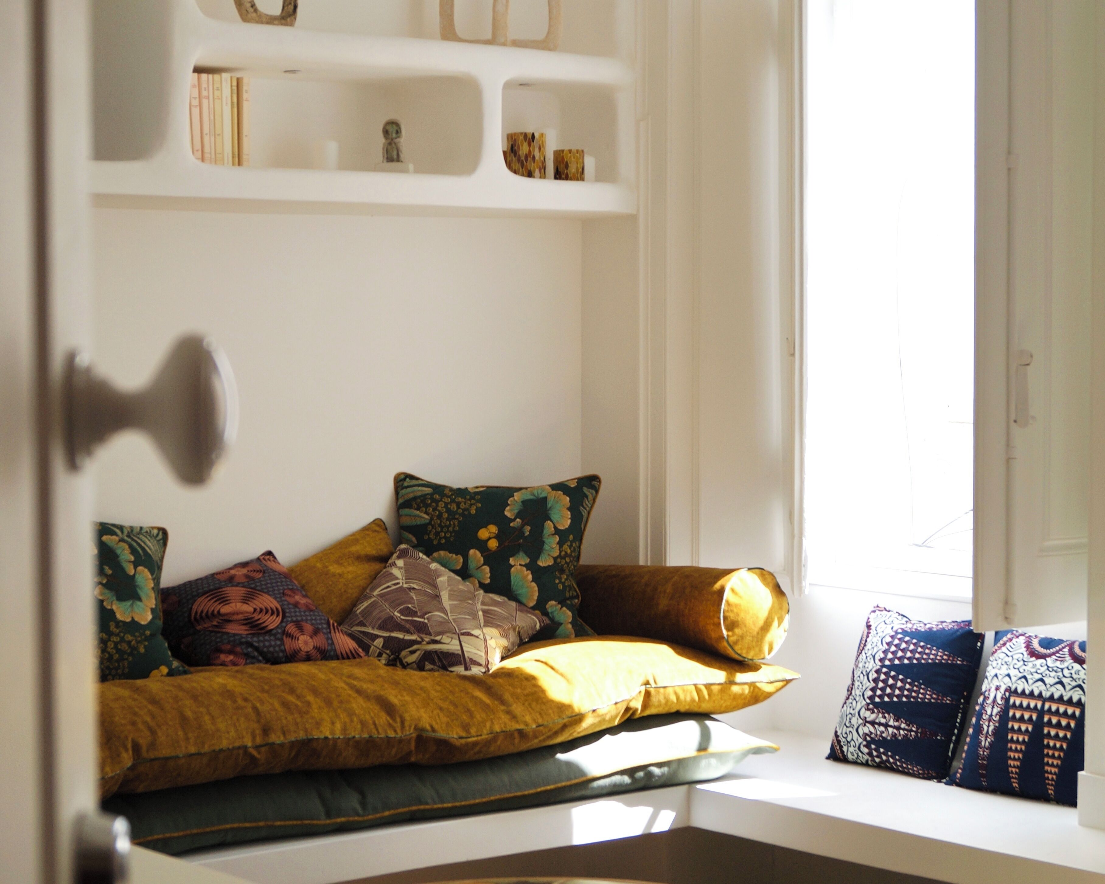 A cozy seating area with a cushioned bench, a variety of pillows, and a bookshelf with books and decorative items.
